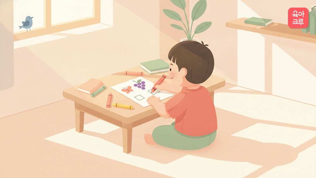 낮은 책상에서 아이가 색연필로 그림 옆 글자 칸을 채우는 한글 학습지 그림